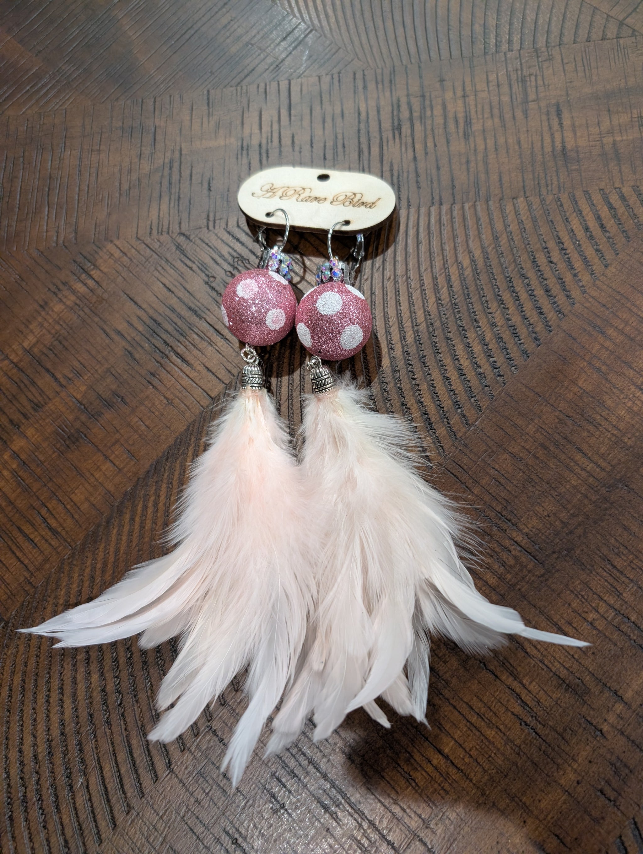 A Rare Bird Pink Glitter Bead Feather Earrings on branded wooden card