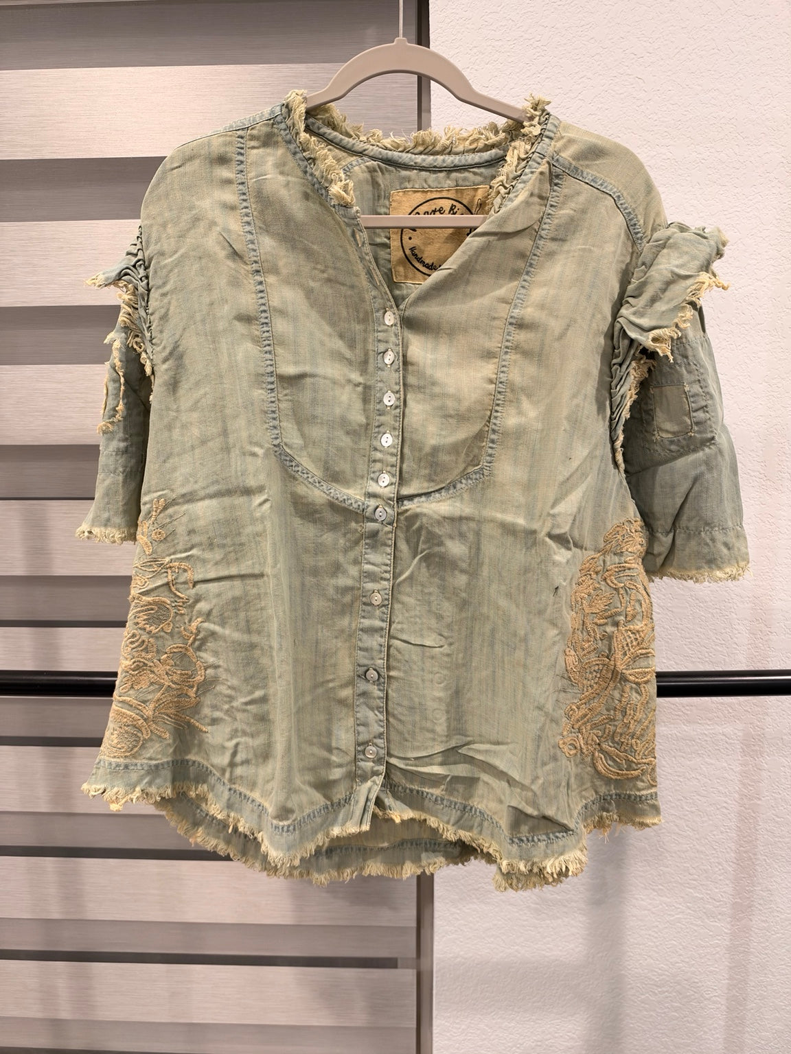 A Rare Bird sage green embroidered button-front top with ruffled sleeves and frayed edges, front view