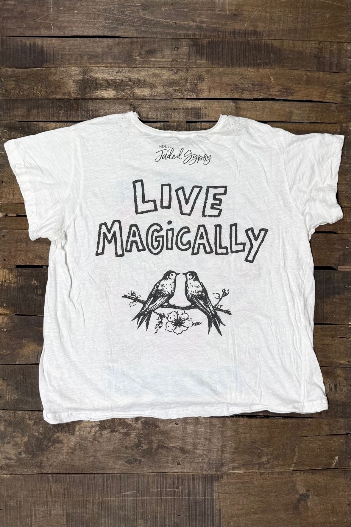 Back of House of Jaded Gypsy Weathered and Worn Tee Derby with Live Magically lettering, two birds on a flowering branch and brand logo