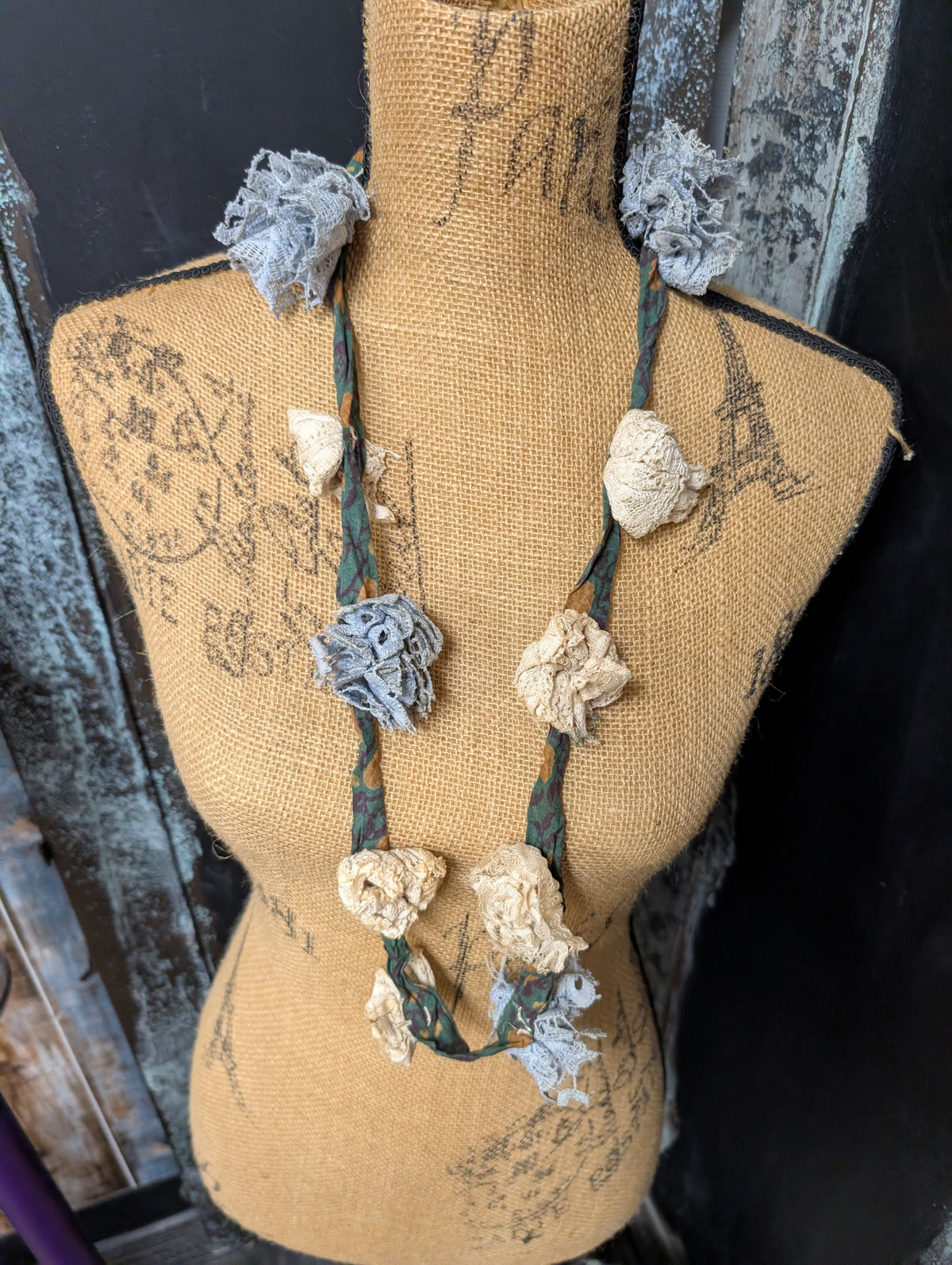 Design B cloth flower necklace with blue and cream flowers on a teal printed fabric strand