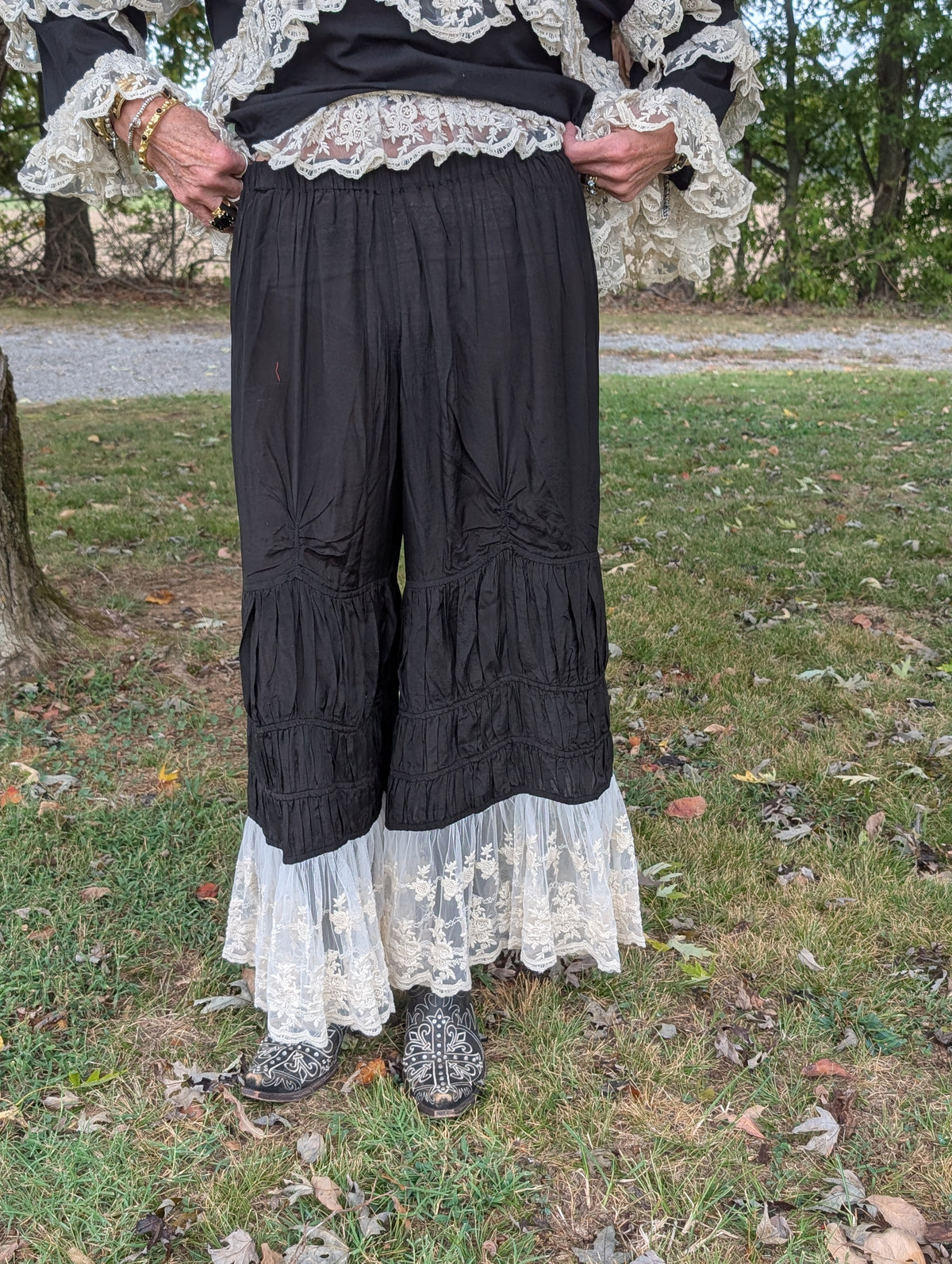 Rambling Rose Lace Pants in Black — front view showing a gathered waist, ruched details, tiered legs and light floral lace hems.